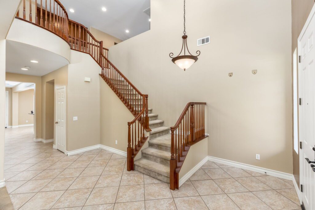 Bright foyer showcasing a curved staircase with wooden railings, tile flooring, and a decorative hanging light fixture, conveying elegance and openness.