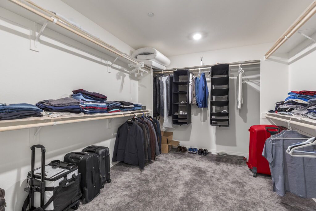 Organized walk-in closet featuring neatly folded clothes on shelves, hanging garments, and luggage, showcasing efficient storage solutions.