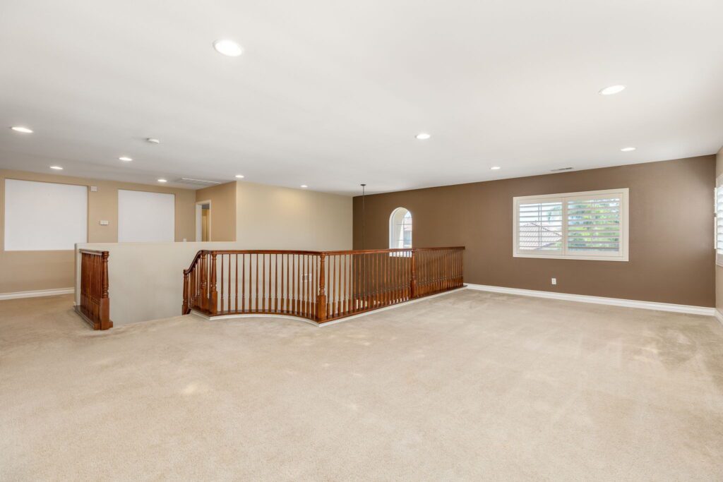 Bright, spacious upper landing with a wooden banister, beige carpeting, and large windows providing natural light. Ideal for showcasing property interior.