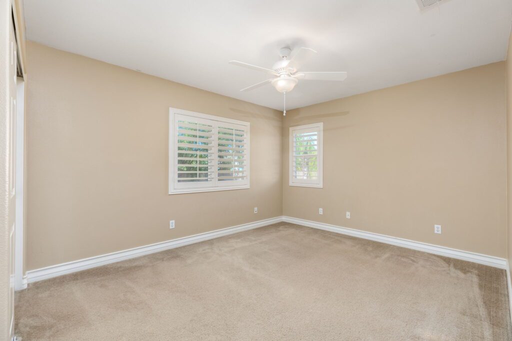 Bright, spacious bedroom featuring neutral walls, carpeted floor, and two windows with white shutters. Ideal for showcasing potential living space.