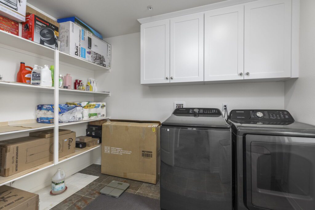 Laundry room featuring a black washer and dryer, shelves stocked with cleaning supplies, and stacked boxes, emphasizing organization and utility.