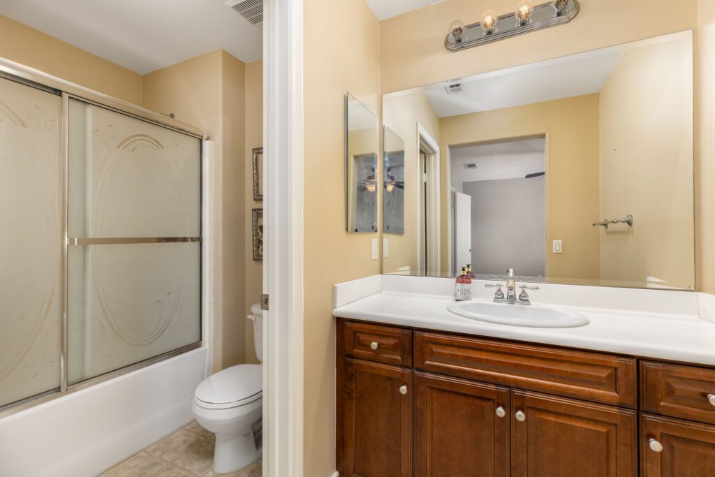 Bright, clean bathroom featuring a wooden vanity with a sink, a glass shower door, and a white toilet. Decorated with mirrors and light fixtures.