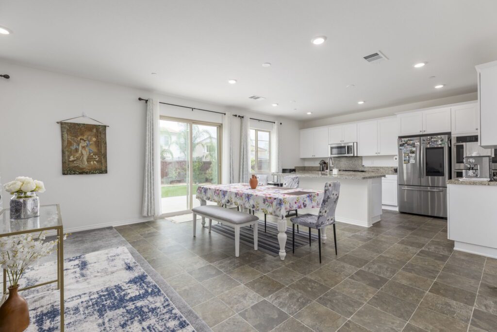 Bright, modern kitchen and dining area featuring a floral tablecloth, stainless steel appliances, and sliding glass doors to a backyard.
