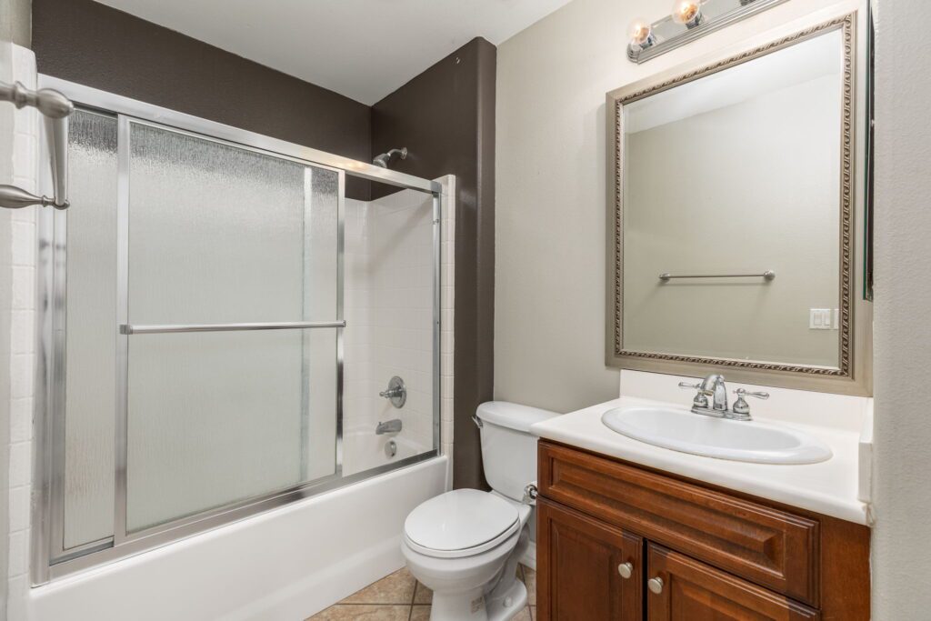 Modern bathroom featuring a glass shower with sliding doors, a white toilet, and a wooden vanity with a sink and mirror.