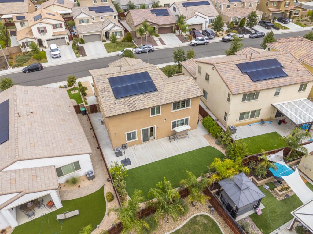 Aerial view of suburban homes with solar panels, showcasing well-maintained yards and driveways. Highlights residential energy efficiency and landscaping.