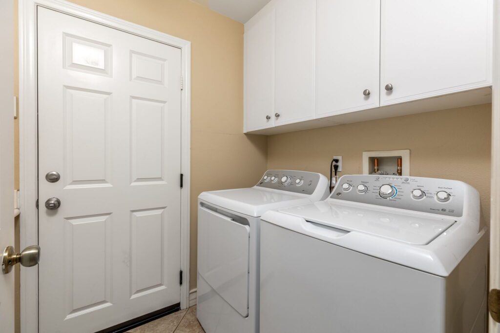 Laundry room featuring a white washer and dryer side by side, with cabinetry above and a closed white door in the background.