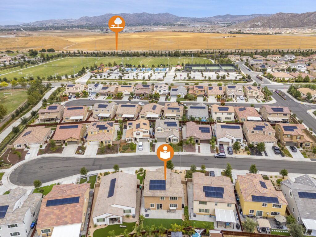 Aerial view of a suburban neighborhood featuring houses with solar panels, adjacent park and sports facilities. Highlights key community amenities.