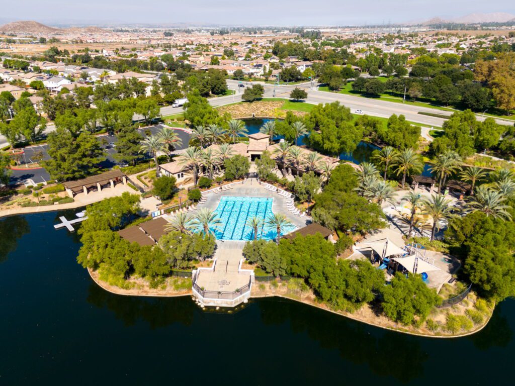 Aerial view of a community pool surrounded by palm trees and greenery, with homes and roads in the background, highlighting a recreational area.