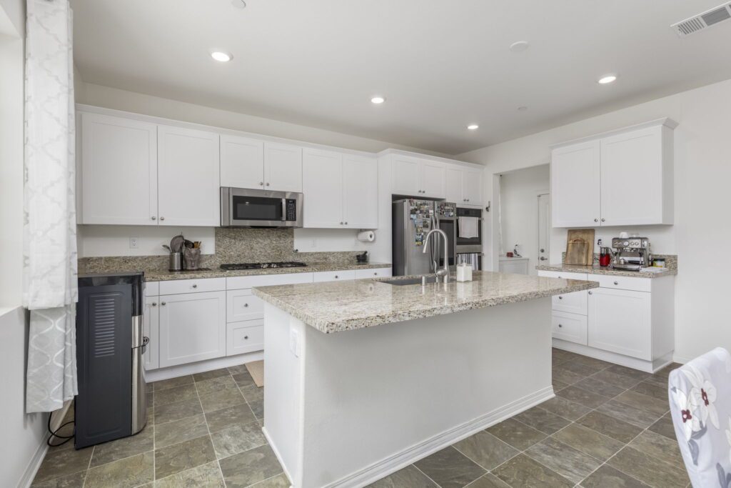 Modern kitchen featuring white cabinetry, granite countertops, stainless steel appliances, and a central island, ideal for cooking and gatherings.