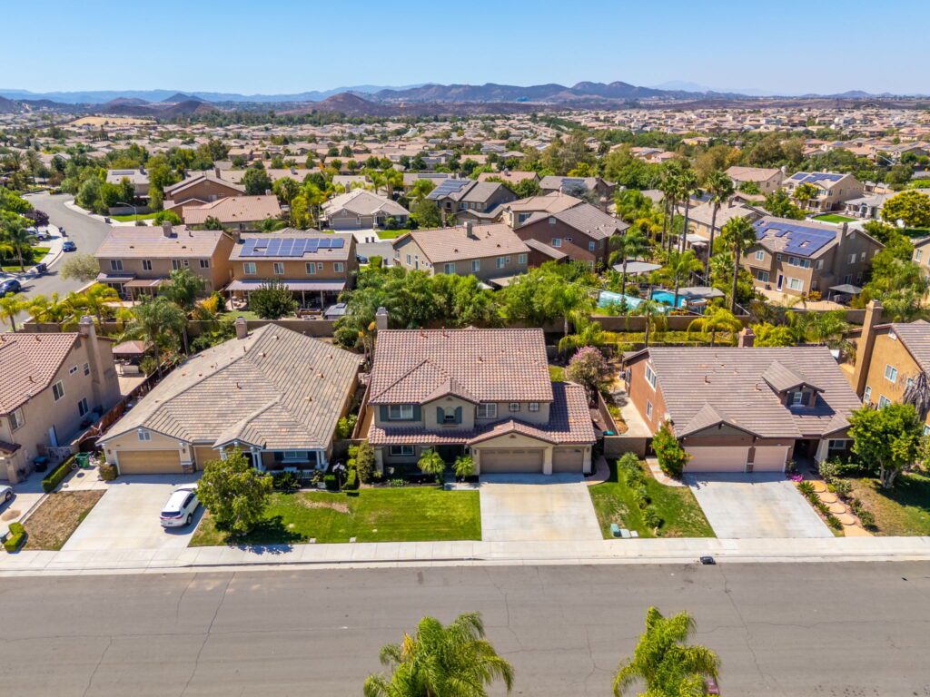 Aerial view of suburban homes with solar panels, lush gardens, and a clear blue sky, showcasing a thriving residential neighborhood.