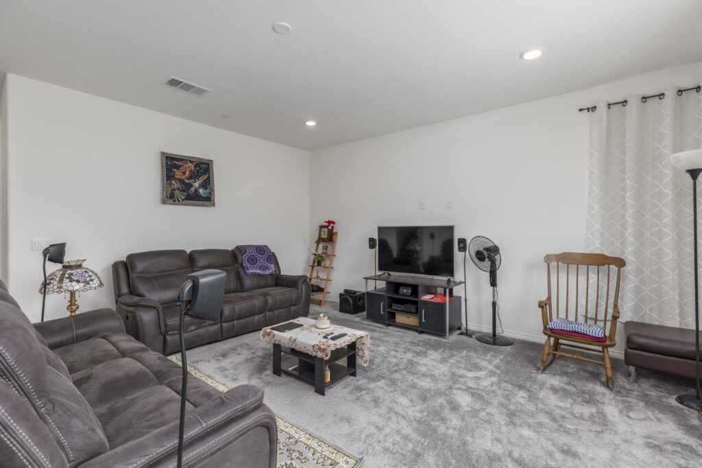 Cozy living room featuring dark leather sofas, a wooden rocking chair, a TV stand with a flat-screen TV, and decorative wall art.