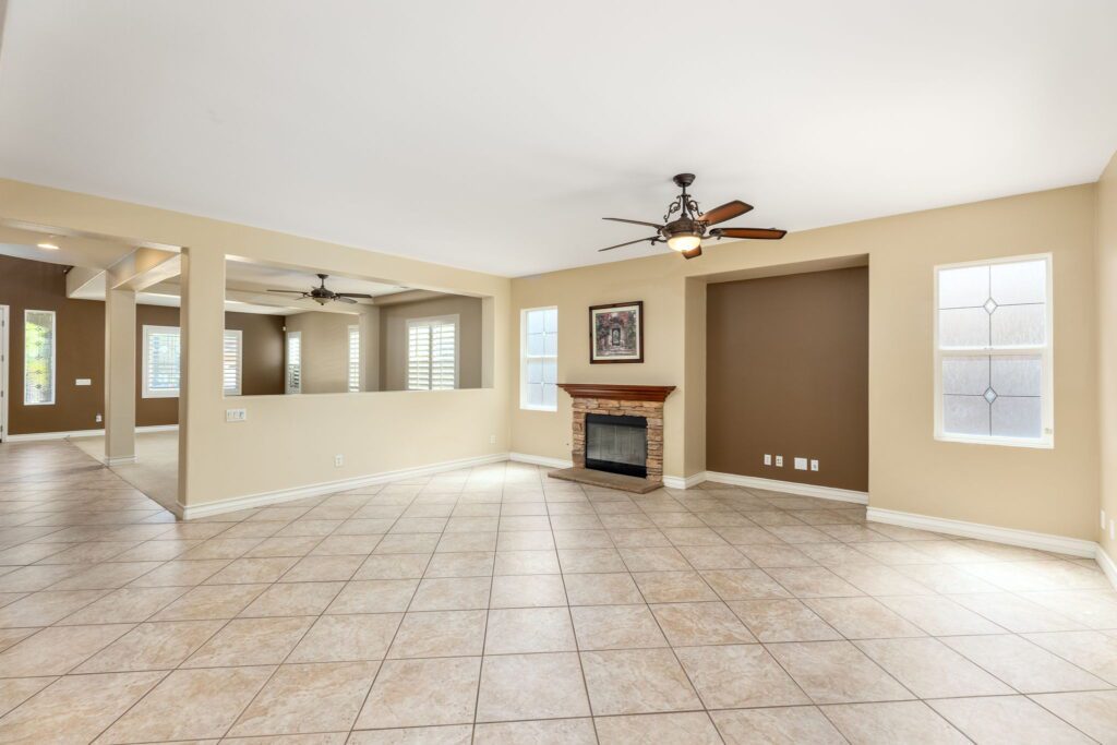 Spacious living area featuring a ceiling fan, tiled floor, and a stone fireplace, with large windows providing natural light. Ideal for showcasing home design.