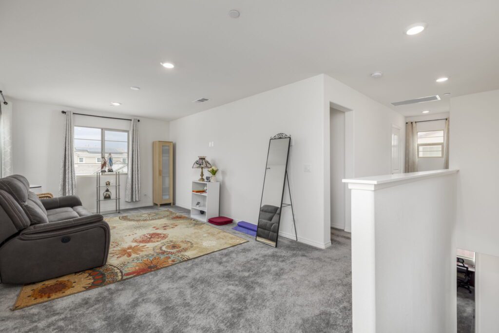 Spacious living area featuring a plush rug, modern furniture, and natural light from large windows, showcasing a cozy and inviting atmosphere.