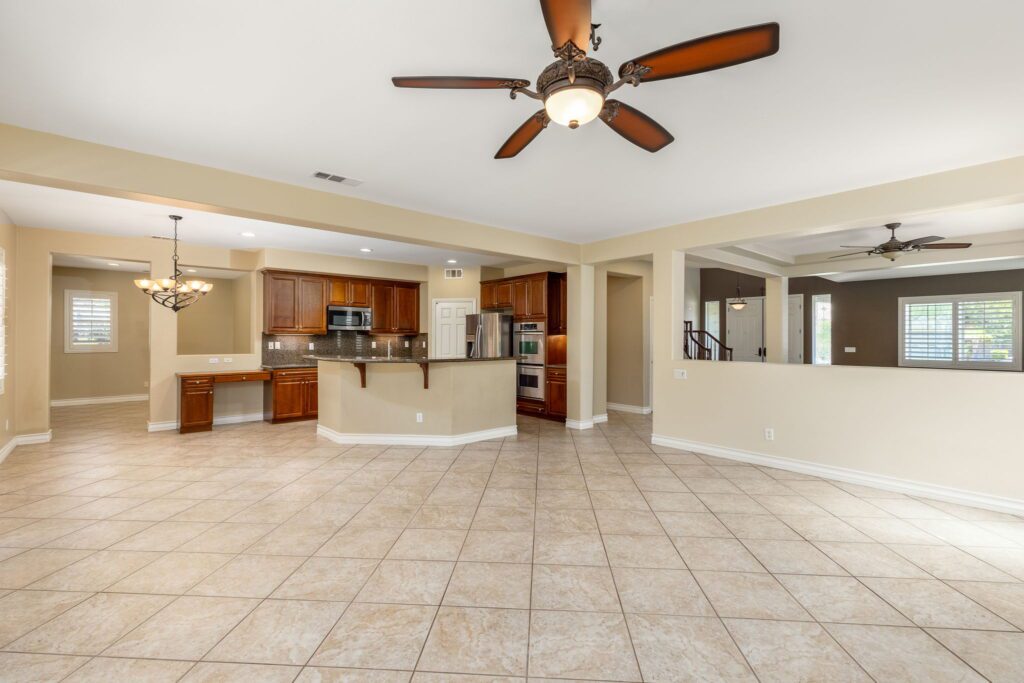 Spacious open concept living area featuring tiled flooring, modern kitchen with wooden cabinets, and decorative ceiling fan. Ideal for entertaining.