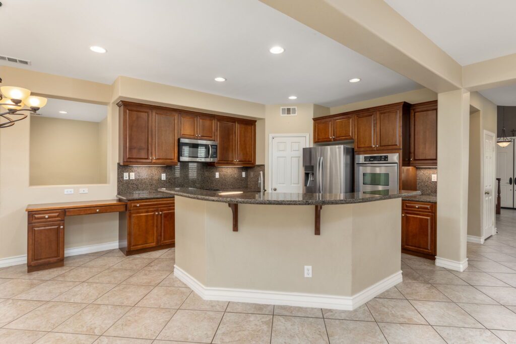 Modern kitchen with wood cabinets, granite countertops, stainless steel appliances, and a breakfast bar, showcasing spacious and functional design.