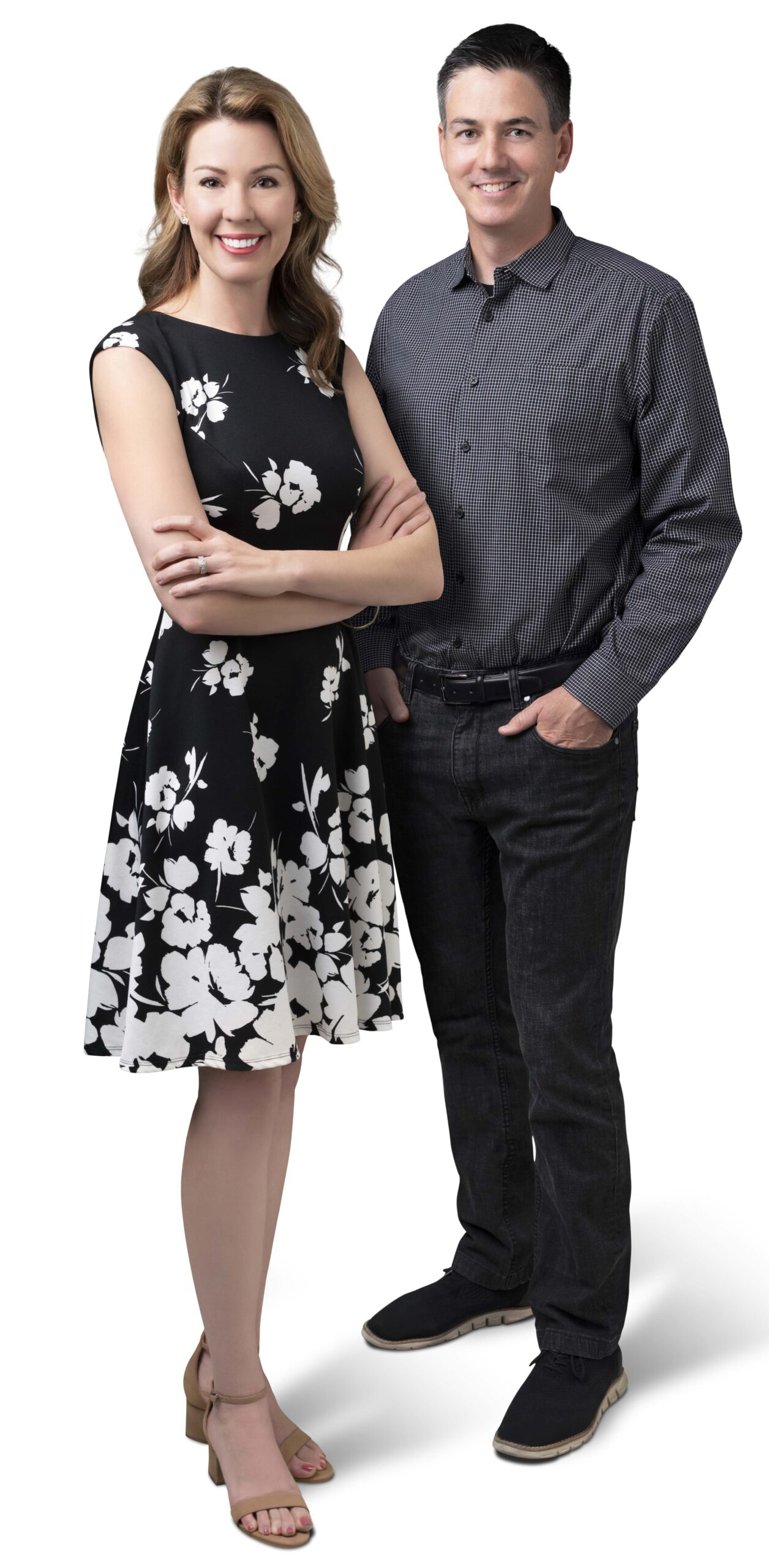 A woman in a floral black dress and a man in a checkered shirt stand side by side, smiling confidently against a plain background.