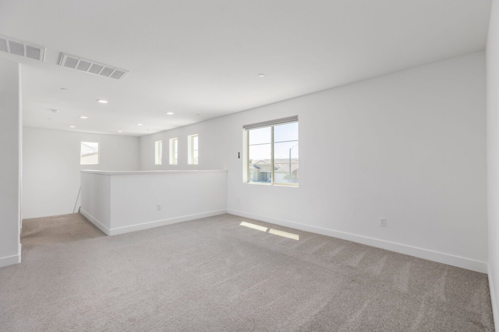Bright, spacious living area featuring light gray carpet, white walls, and multiple windows, creating an airy atmosphere ideal for potential homebuyers.