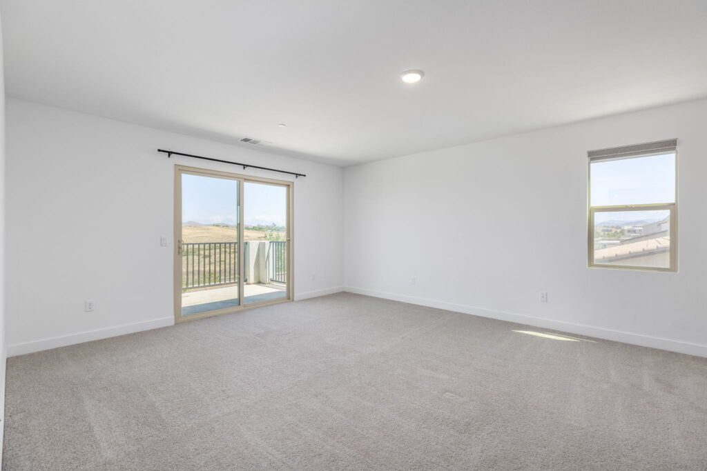 Spacious, empty room with light gray carpet, large sliding glass doors leading to a balcony, and a window with scenic outdoor views.