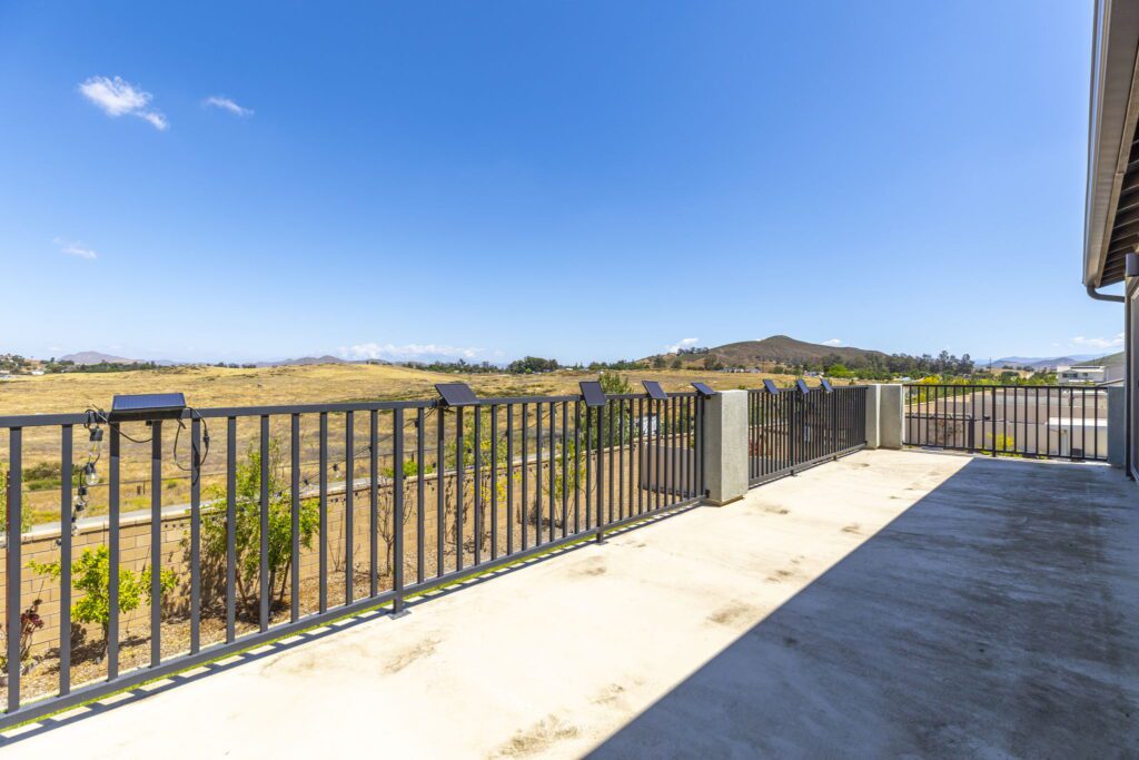 Spacious balcony overlooking expansive hills and clear blue sky, featuring solar lights along the railing. Ideal for outdoor relaxation.