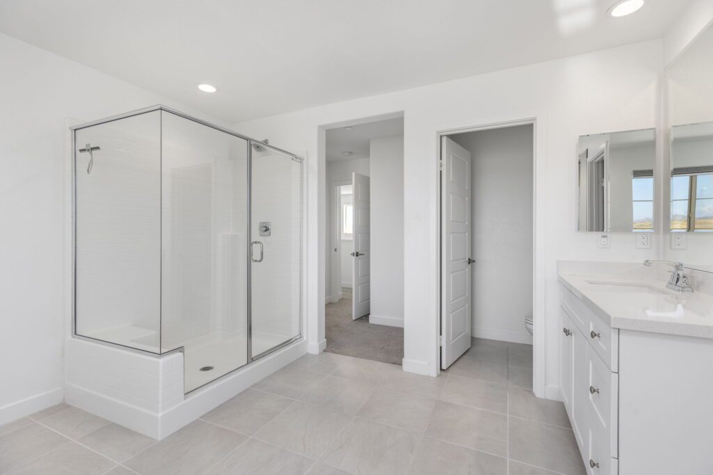 Modern bathroom featuring a glass shower enclosure, double vanity with mirrors, and light-colored tiles. Bright and spacious design.