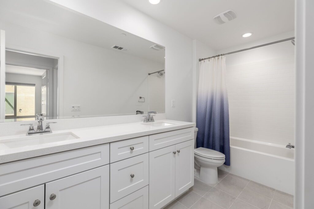 Bright, modern bathroom featuring a white vanity with a sink, a bathtub with a white tiled surround, and a blue gradient shower curtain.