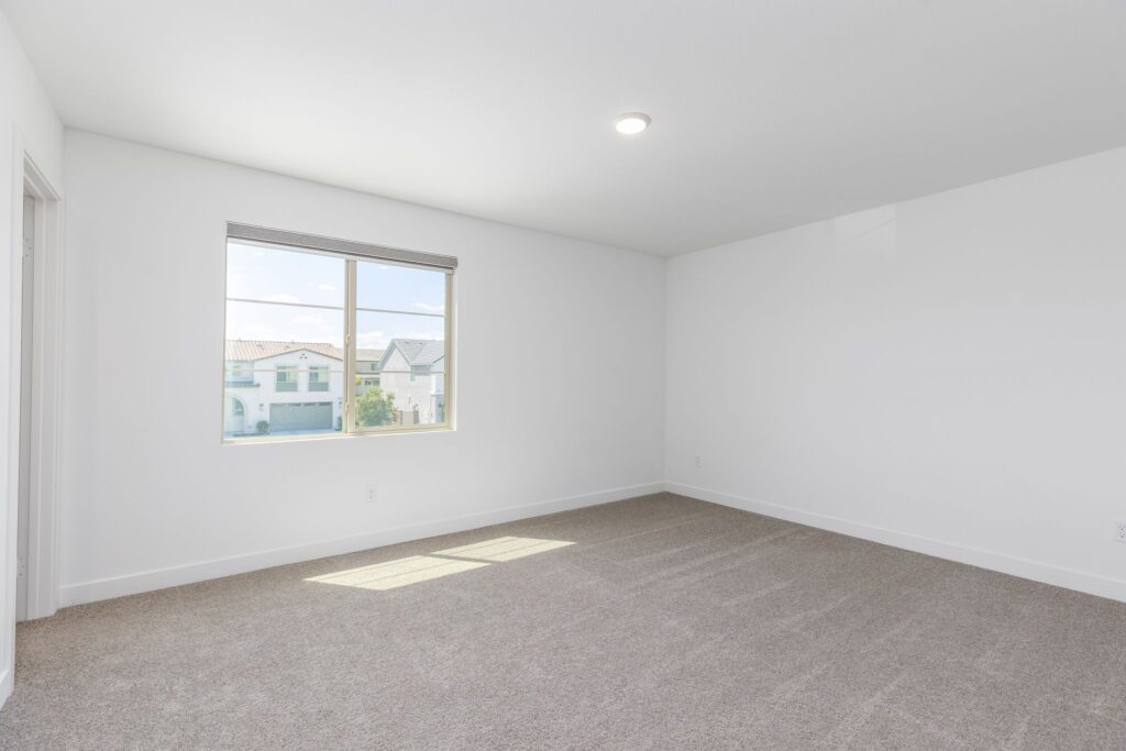 Spacious, empty room with carpet and a large window letting in natural light, ideal for showcasing potential living space.
