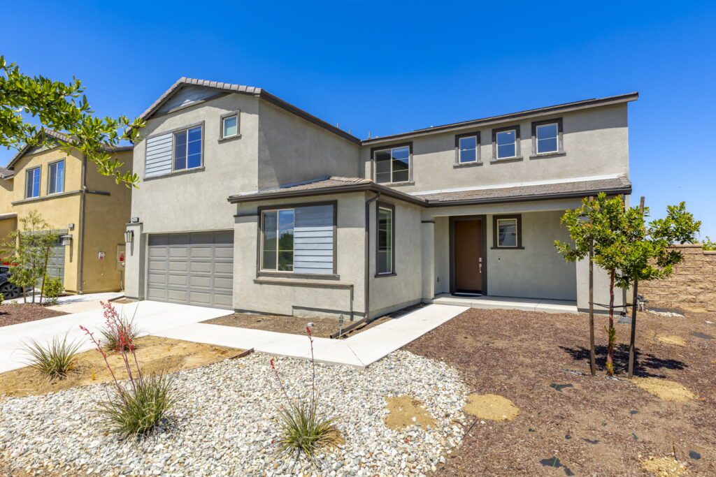 Modern home exterior featuring a beige stucco finish, a two-car garage, and landscaped front yard. Clear blue sky provides a bright backdrop.