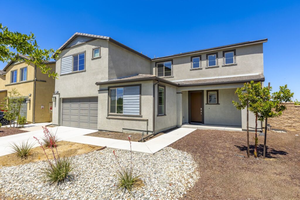 Modern home exterior featuring a beige stucco finish, a two-car garage, and landscaped front yard. Clear blue sky provides a bright backdrop.