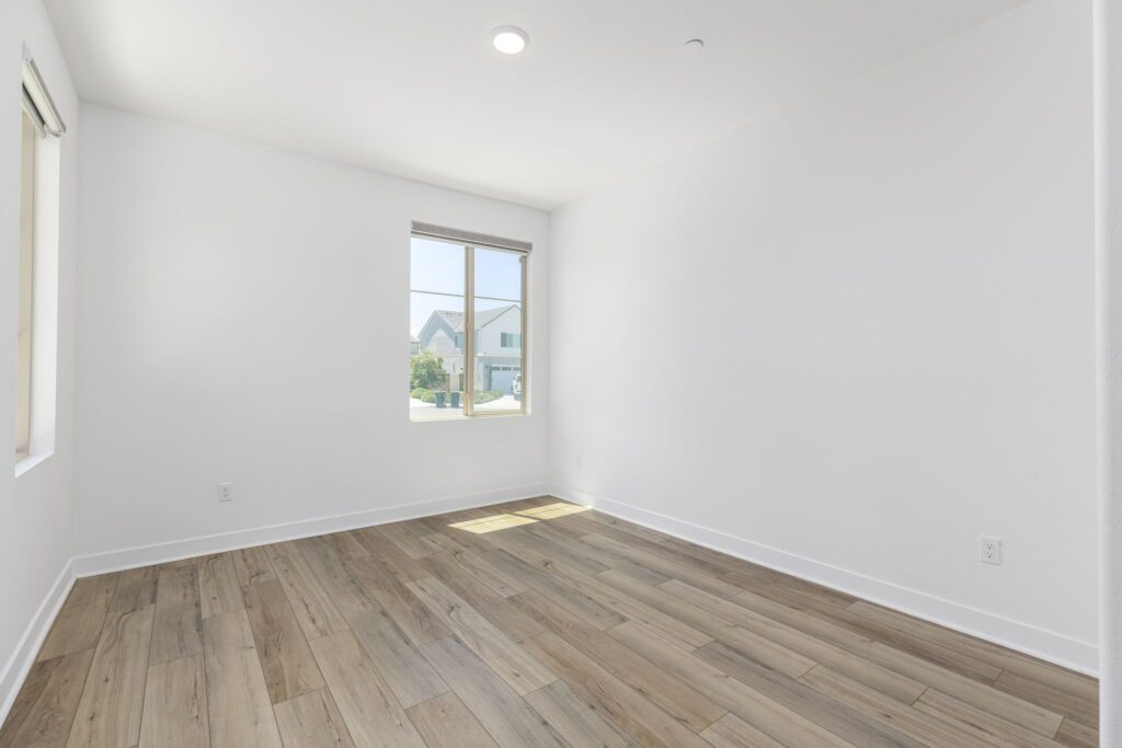 Spacious, sunlit room featuring light wood flooring and a window framing a neighborhood view. Ideal for interior design inspiration.