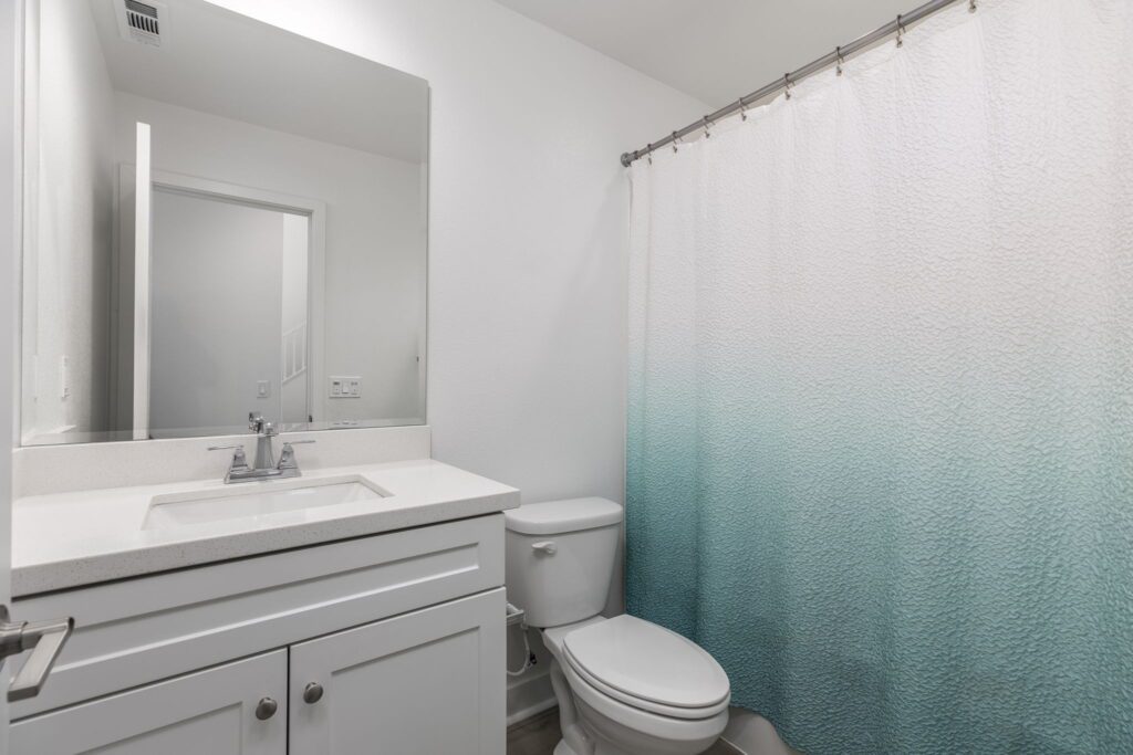 Bright, modern bathroom featuring a white vanity, a large mirror, and a teal ombre shower curtain, emphasizing a clean and inviting space.