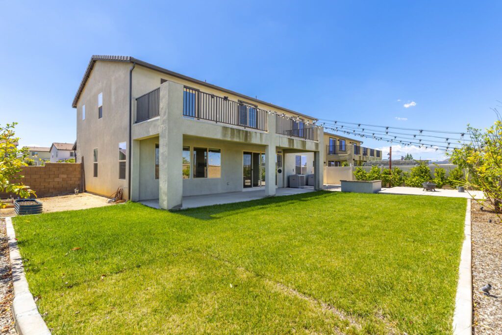 Modern two-story home with a large backyard, green lawn, and patio area. Clear blue sky enhances the outdoor living space. Ideal for family gatherings.