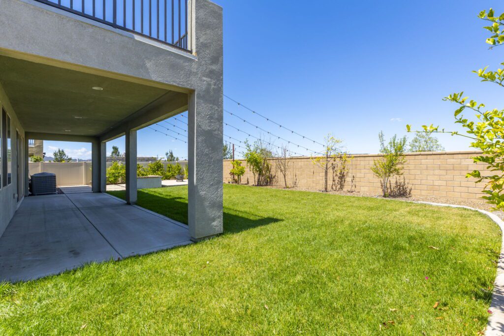 Lush green backyard featuring a covered patio, landscaped border, and decorative string lights overhead, ideal for outdoor gatherings.