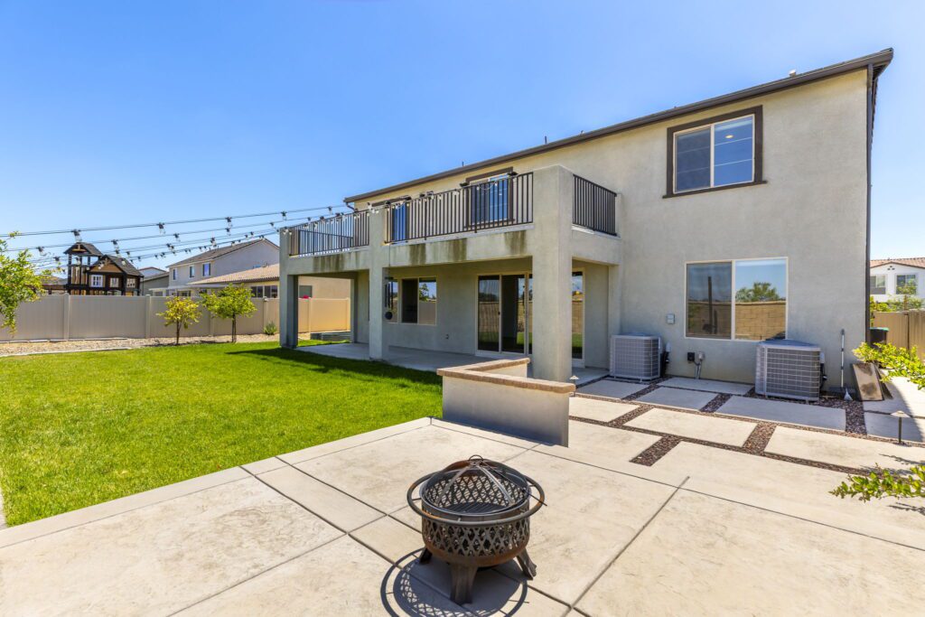 Modern two-story home exterior featuring a backyard with a green lawn, patio area, and outdoor seating. Ideal for outdoor entertaining.