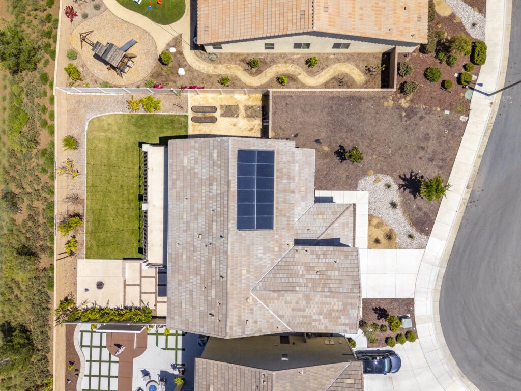 Aerial view of a residential area featuring a house with solar panels, landscaped yards, and a playground, highlighting outdoor living spaces.