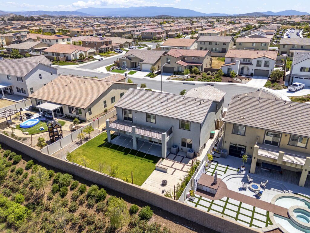 Aerial view of suburban homes with landscaped yards, featuring a house with a pool and patio area, showcasing the residential layout and neighborhood structure.