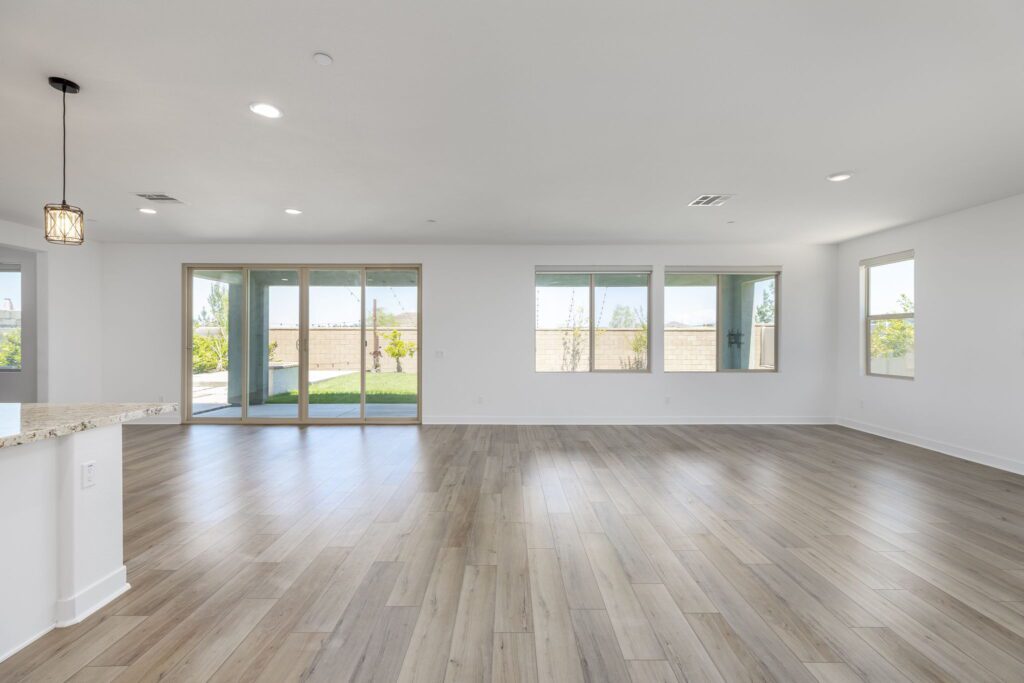Spacious, sunlit living area featuring light wood flooring, large windows, and sliding doors leading to a backyard. Ideal for modern living.