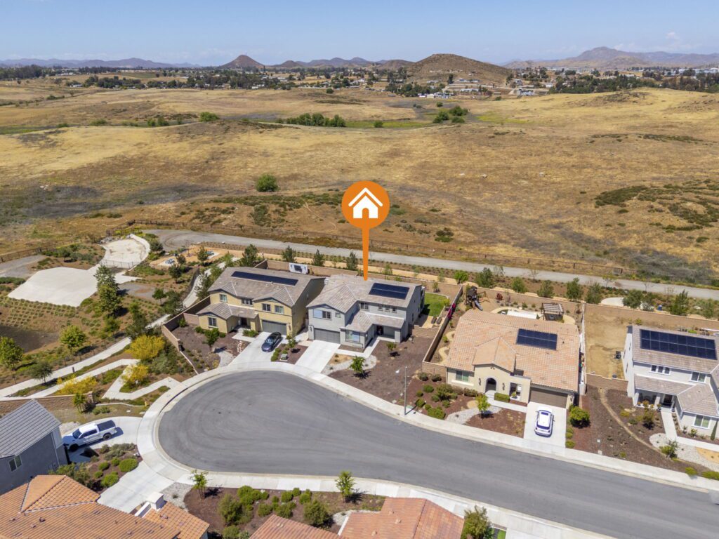 Aerial view of a residential neighborhood featuring homes with solar panels, surrounded by open fields and hills in the background, highlighting available properties.