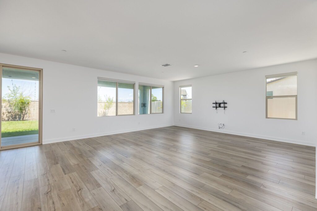 Spacious, empty living room featuring large windows for natural light, hardwood flooring, and a wall-mounted TV bracket, perfect for design inspiration.