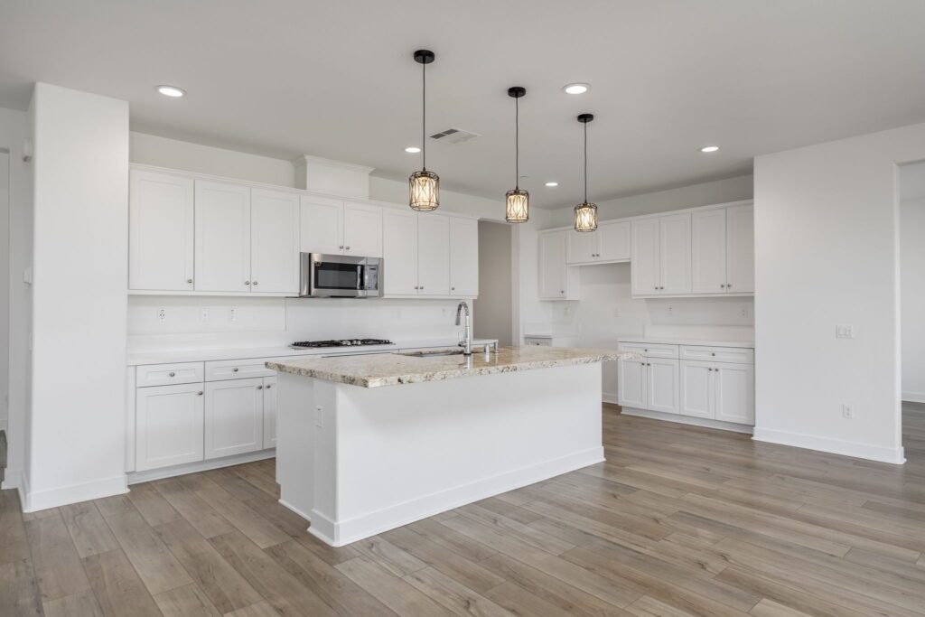 Modern kitchen featuring white cabinetry, a large island with a granite countertop, and pendant lighting. Bright and spacious layout.