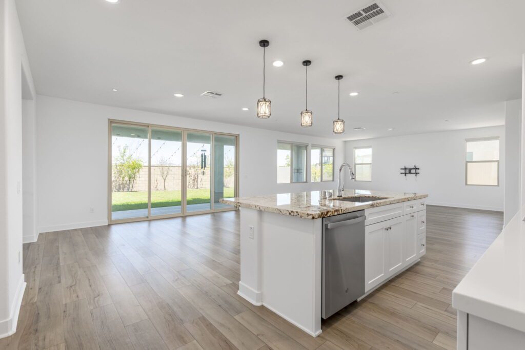 Modern open-concept kitchen featuring a granite island, stainless steel appliances, and large sliding glass doors leading to a backyard.