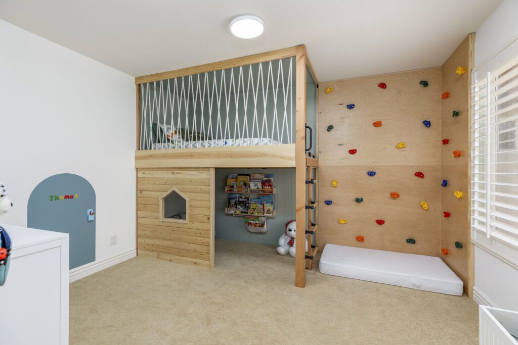 Children's playroom featuring a wooden loft bed with a climbing wall. Below, a cozy reading nook and a small playhouse invite imaginative play.
