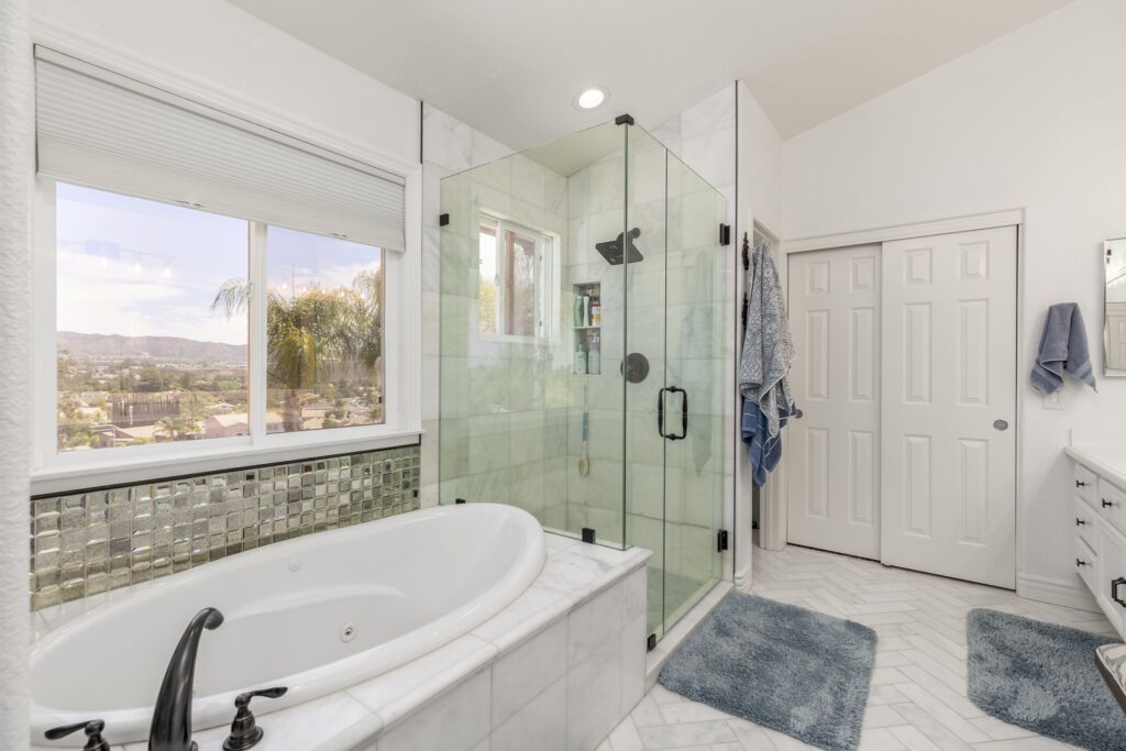 Modern bathroom featuring a freestanding tub and glass shower, with scenic mountain views through a large window. Soft blue accents enhance the decor.