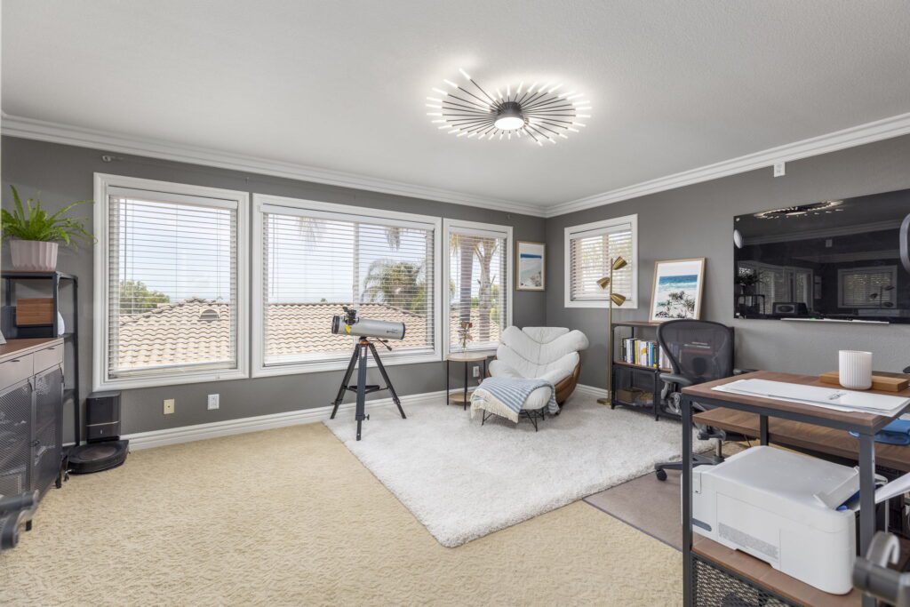 Cozy home office with modern decor, featuring large windows, a telescope, and a comfortable chair, offering a relaxed workspace with natural light.