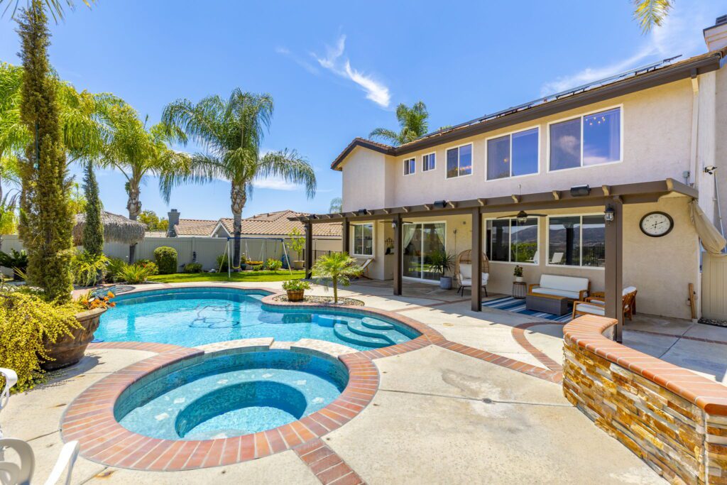 Bright backyard oasis featuring a sparkling pool and a spa, surrounded by palm trees. Ideal for relaxation and outdoor gatherings.