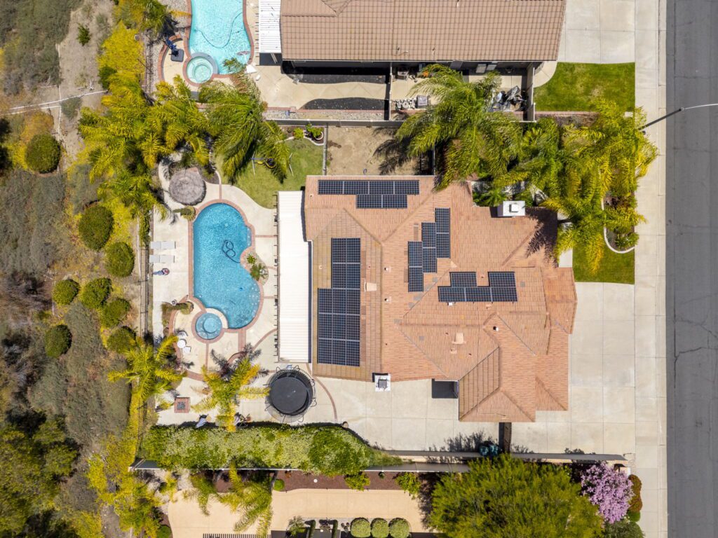 Aerial view of a villa featuring a swimming pool, jacuzzi, and solar panels on the roof, surrounded by palm trees and landscaped gardens.