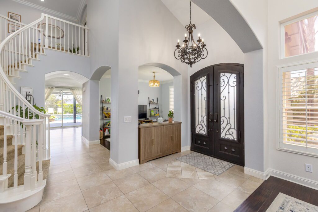 Elegant entryway showcasing a spiral staircase, stylish chandelier, and double doors leading to a bright outdoor area with a pool.