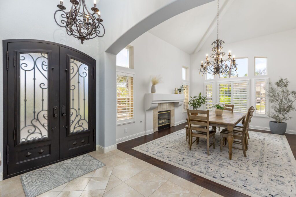 Elegant open entryway featuring double doors, a chandelier, and a wooden dining table surrounded by chairs, enhancing the inviting atmosphere.